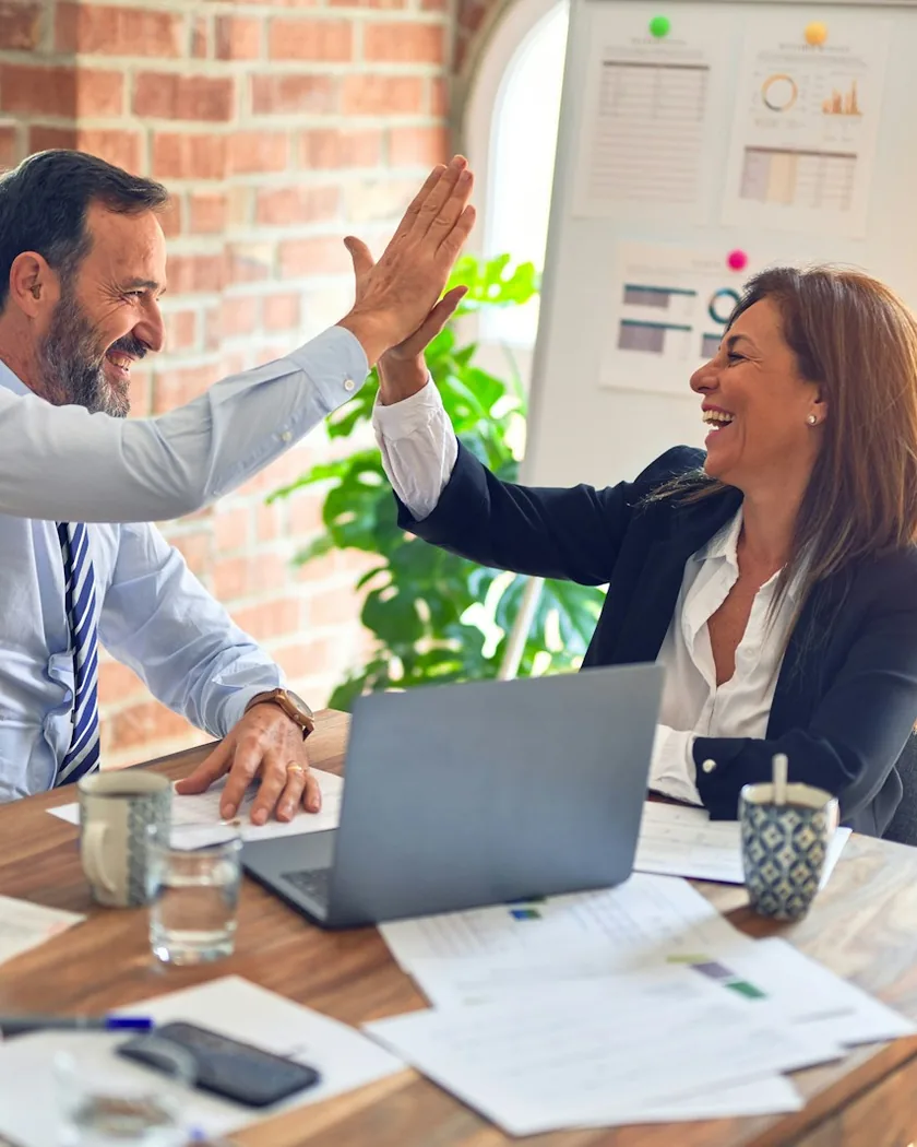 Stock photograph of two colleagues celebrating over a laptop at a desk
